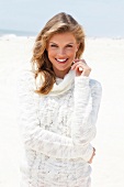 Portrait of blonde woman wearing white turtleneck sweater standing on beach, smiling