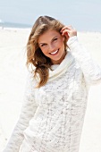 Portrait of blonde woman wearing white turtleneck sweater standing on beach, smiling