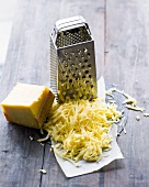 Grated cheese with piece of cheese and grater on wooden surface