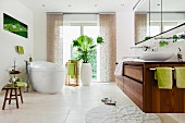 Grosszügiges Badezimmer in Weiß mit freistehender Badewanne, Waschbeckenunterschrank aus Holz & grünen Farbakzenten