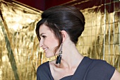 Pretty woman with dark hair in 70s style updo looking sideways, smiling widely