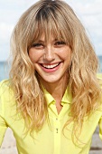 Portrait of cheerful blonde woman wearing yellow shirt sitting on beach, smiling