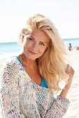 blonde Frau im hellen Pulli lächelt in Kamera, am Strand