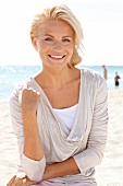 Portrait of happy woman wearing bright top sitting on beach, smiling