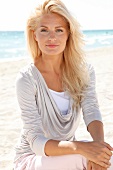 Portrait of happy woman wearing bright top sitting on beach, smiling