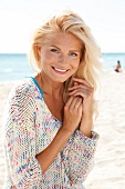 blonde Frau im hellen Pulli lächelt in Kamera, am Strand