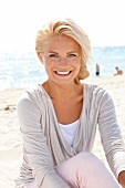 Portrait of happy woman wearing bright top sitting on beach, smiling