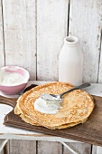 Sour cream with pancakes on chopping board