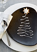 A plate decorated for Christmas with a writing icing Christmas tree and a cinnamon star biscuit on top