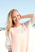 Blonde woman in a white sweater on the beach, smiling at camera