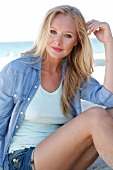 Blonde woman in a denim shirt smiles at the camera on the beach