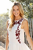 Blonde woman with long hair in a summer dress on the beach in front of a fence