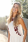 Blonde Frau mit langen Haaren in Sommerkleid am Strand vor Zaun