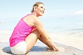 Blonde Frau mit langen Haaren im pinken Shirt relaxt am Strand