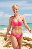 Blonde Frau mit kurzen Haaren im pinkfarbenem Bikini am Strand