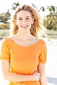 Blonde Frau mit langen Haaren in orangefarbenem T-Shirt am Strand