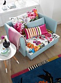 Sessel mit bunten, floral gemusterten Kissen, Retro Beistelltisch und gemusterter Teppich in einem Wohnzimmer