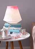 A table lamp made from coloured rice paper on a bedside table with books and porcelain cups