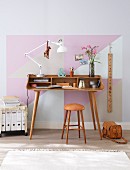 A delicate home office desk made from curved, laminated wood and a ringbinder trolley with the wall painted with pastel-coloured triangles