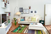 Weisses Medienmöbel und Hängeregale zu cremefarbenem Sofa mit Ottomane, gestreifter Teppich