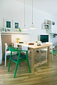 A dining area in an open plan living room, a simple solid wood table with white chairs and one green chair