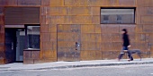 Mann mit Hund spazieren an Hausfassade mit rostigen Cortenstahlplatten vorbei