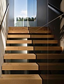 Schmales Treppenhaus mit offenen Holzstufen und schwarzen Steinfliesen an Wand