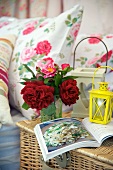 A small bunch of flowers, lanterns and a book on top of a picnic basket next to bed