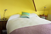 Ein Doppelbett in einem gelben Schlafzimmer im Dachgeschoss