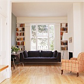 Black sofa beneath a window and antique chair with checked upholstery in an open living room