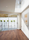 Corner of a minimalist room with skylight and sliding patio doors with a view of boxwood trees