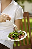 A woman eating spinach salad with veal fillet