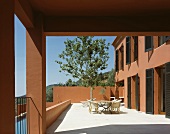 Sun-drenched terrace with table and chairs in front of a tree and a Mediterranean home with a reddish brown facade