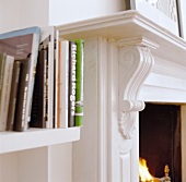 Detail of white shelves with books beside a chimney with a carved, white lacquered mantelpiece