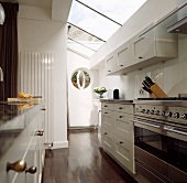 Kitchen with skylight strips above a white lacquered hanging cupboards and stainless steel oven on dark wood flooring