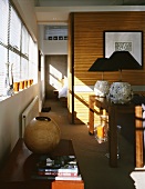 Round vases on a chest and table lamps with black shades in a dining room with a view through a ceiling high doorway