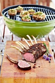 Grilled lamb rack with a barbecue in the background
