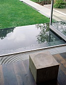 Stool made of solid wooden cube in front of open terrace door and wet terrace floor