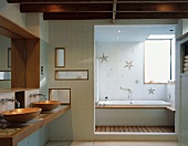 Waschtisch mit Schüsseln aus Holz und Durchgang zur Badewanne mit Seesternenmuster auf Fliesen