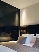 Cushions on double bed with upholstered head next to black, reflective wall