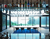 Bar with liquor and glasses on suspended shelves and view of a dining table in front of a glass facade
