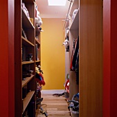 Built-in shelves and open cupboard in a dressing room with a view of a yellow wall