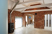 Living room in a converted barn with brick wall and openings with round arches under a white lacquered wood ceiling an wood burning stove
