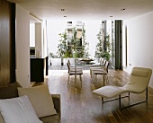 Open living room with white leather lounger in front of a dining table with chairs and a view of the terrace