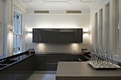 Counter with champagne glasses on a tray in a designer kitchen with brown, glossy cabinets in a stately home