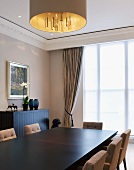 Dark dining table with upholstered chairs under a hanging lamp with a gold shade in front of a window