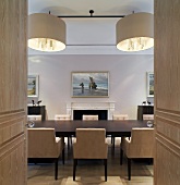 Blick durch offene Flügeltür auf Tafel mit gepolsterten Stühlen und Designerhängelampe im Esszimmer