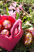 Chocolate Easter eggs in a pink felt basket in a meadow