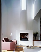 Pink armchair in front of a fire in a fireplace in an open, minimalist living room