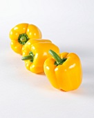 Three yellow peppers on a white surface